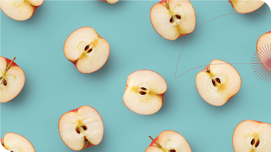 Várias maçãs cortadas ao meio sobre uma superfície azul.