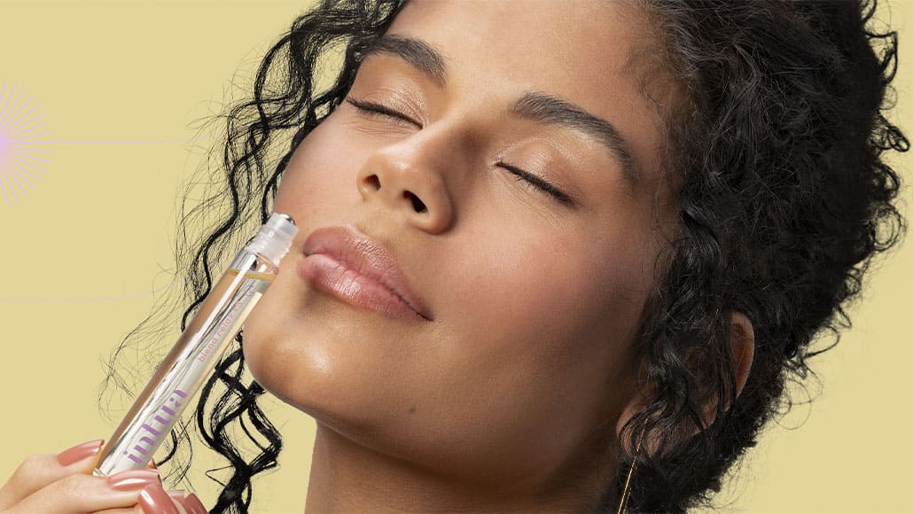 Mulher com os olhos fechados cheirando o roll-on Blend Relax de aromaterapia da Intua.