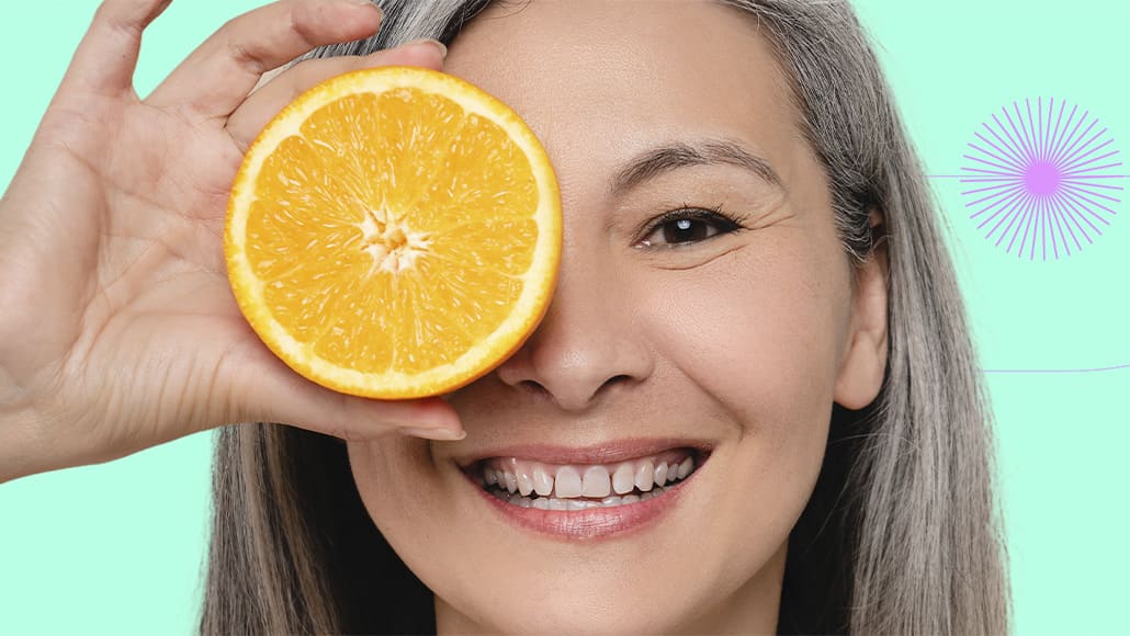 Mulher segurando uma laranja sobre um olho e sorrindo