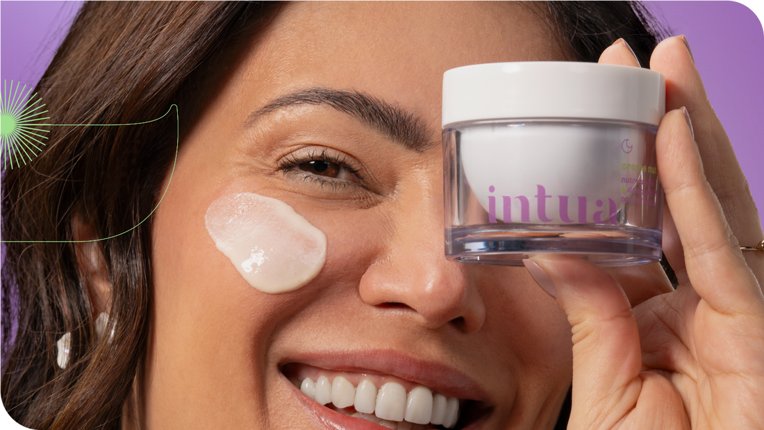 mulher sorrindo segurando um vidro do Creme Nutritivo Facial sobre um olho e um pouco do produto está aplicado em sua bochecha