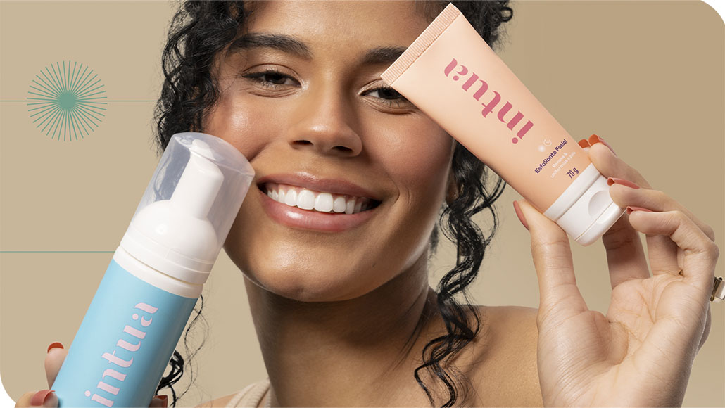 mulher sorrindo segurando a Espuma de Limpeza Facial e o Esfoliante Facial da Intua sobre seu rosto