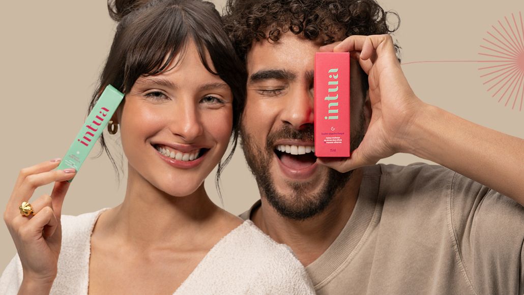 Mulher sorrindo e segurando um Sérum Soft Focus ao lado de um homem segurando um Balm Desinchaço sobre os olhos.