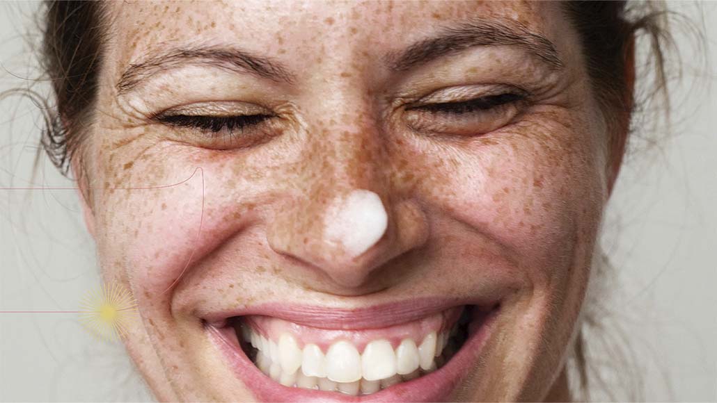 mulher com manchas na pele sorrindo, com o Creme Nutritivo Facial da Intua aplicado em seu nariz